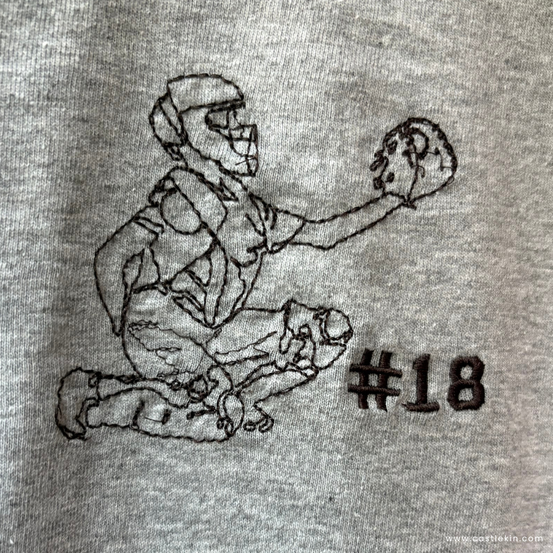 Embroidered design of a softball catcher on a gray sweatshirt with player #18 embroidered on the side.